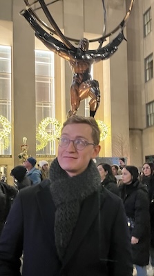 Liam standing in front of the bronze statue of Atlas in Rockefeller Center. It looks like Atlas is standing on top of Liam's head.